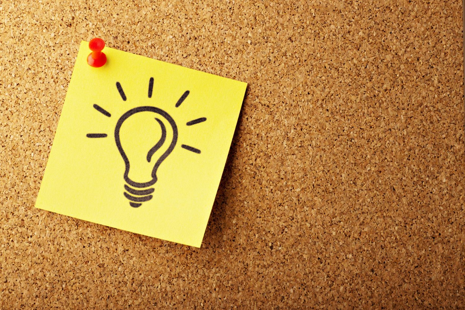 Sticky note with a hand-drawn lightbulb pinned to a corkboard